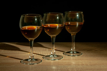 Three glasses with calvados stand on the table against black background