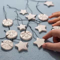 Cute baby toddler hand holding small ornament pendant figure, made of self drying white clay and shining glitter. Shallow depth of focus, bokeh effect on blue background, stars and round shapes.