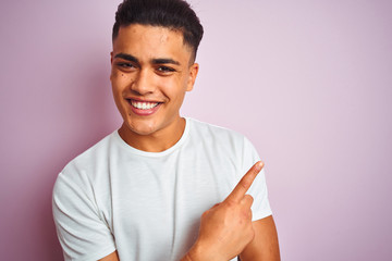 Young brazilian man wearing t-shirt standing over isolated pink background very happy pointing with hand and finger to the side