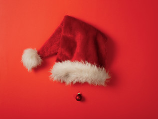 Red Santa Claus hat and Christmas tree toy as nose. Red background. Christmas, New Year and Winter holiday concept photo.