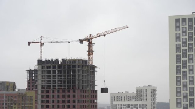 A construction crane lifts a load. Tower Crane on a Construction Site Lifts a Load at High-rise Building. The process of building a multi-story modern residential skyscraper
