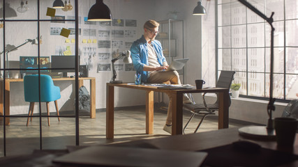 Professional Creative Designer Sits on His Desk Holds Laptop on the Knees Early Morning while Working on the Project. Creative Designe and Gaming Content Development Studio