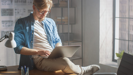 Professional Creative Designer Sits on His Desk Holds Laptop on the Knees and Working on the...