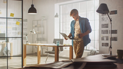 Young Creative Developer is Working in His Studio on a Laptop. Concept of Sucessful Designer working on Application Design, Software UI Development. In the Background Creative Modern Office