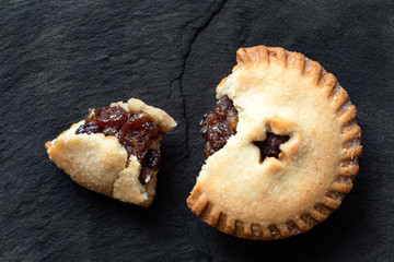 Broken open traditional british christmas mince pie with fruit filling isolated on black slate. Top...
