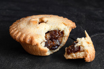 Broken open traditional british christmas mince pie with fruit filling isolated on black slate.
