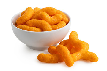 Extruded cheese puffs in a white ceramic bowl next to spilled cheese puffs isolated on white. - obrazy, fototapety, plakaty