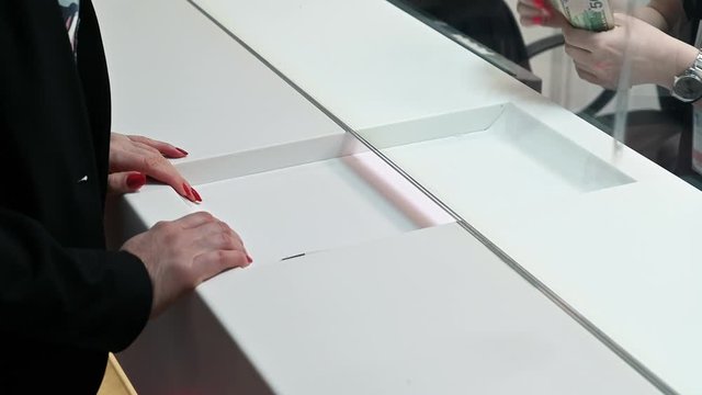 Employee and client count money on a counter at the currency exchange office. Female hand with money in cash department window.
