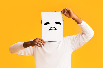 Black man putting paper with sad emoji over his face
