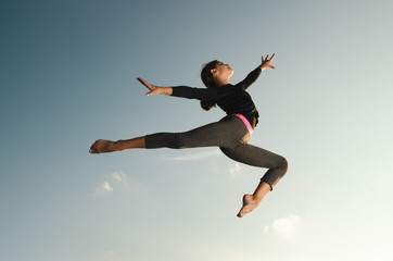 Young girl gymnast acrobat jumping high in the sky