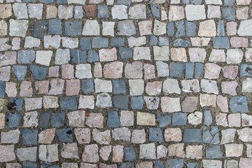 An old damaged stoneblock pavement cobbled with small stone blocks of different colors