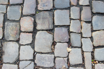 An old stoneblock pavement cobbled with natural stone blocks with gaps between blocks
