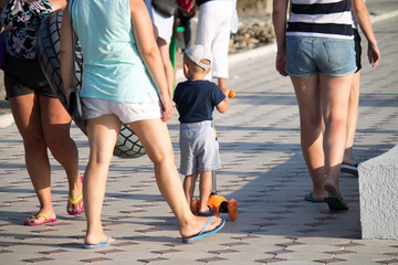 A child with a toy goes to the beach around the feet of adults