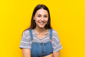 Young woman in dungarees over isolated yellow background laughing