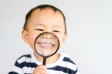 Little toddler boy child holding magnifying glass and showing front teeth with big smile on green grass: Healthy happy funny smiling face young adorable lovely boy kid with new tooth dental.