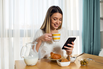 Pretty young woman drinking morning coffee and using phone