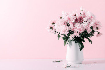 Fresh bouquet of pink flowers in vase on white shelf on pink wall background. Floral home decor.