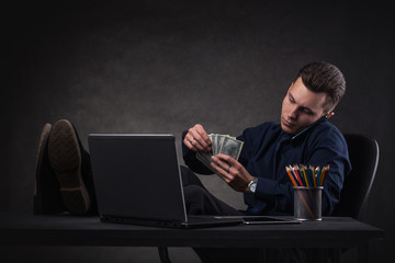 Successful business man at the table on a dark background with laptop and money. Bank Sales Manager