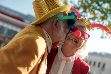 Aged man in clown costume kissing wife outdoors stock photo
