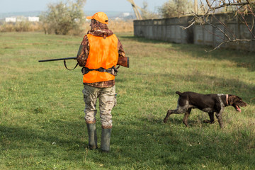 A man with a gun in his hands and an orange vest on a pheasant hunt in a wooded area in cloudy...