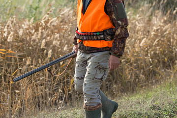 A man with a gun in his hands and an orange vest on a pheasant hunt in a wooded area in cloudy...