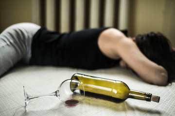 a young girl suffering from chronic alcoholism lies in a dirty room, next to a bottle of wine and a...
