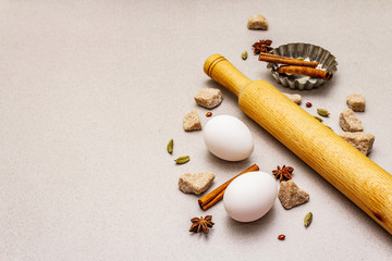 Christmas cooking background, spices, eggs, brown lump sugar, cupcake baking dish and a rolling pin. Light stone concrete background