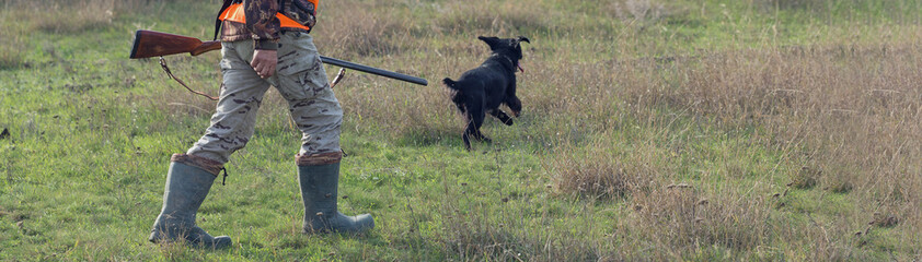 A mans with a gun in his hands and an orange vest on a pheasant hunt in a wooded area in cloudy...