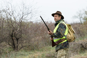 Hunting period, autumn season open. A hunter with a gun in his hands in hunting clothes in the autumn forest in search of a trophy. A man stands with weapons and hunting dogs tracking down the game.