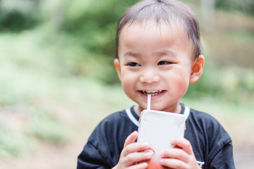 Closeup of little toddler boy drinking milk box with straw in the park.Happy toddler baby boy hungry milk.