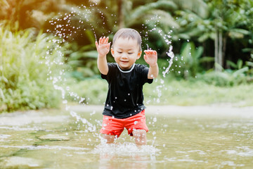 Happy asian toddler boy having fun to play with water in the nature river.He play water and make heart shape in the evening sunlight warm tone.