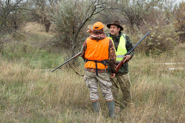 A mans with a gun in his hands and an orange vest on a pheasant hunt in a wooded area in cloudy...
