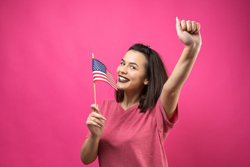 Happy young woman holding American flag against a studio pink background