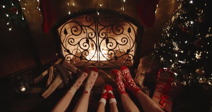 Three pairs of legs in christmas socks lying near fireplace, representing family bonding - christmas spirit concept close up 4k footage