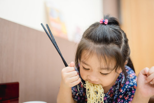 5 Years Old Asian Little Girl Eating And Trying To Use Chopsticks.She Hungry And Delicious Moment Action With Egg Noodles Soup In Chinese Restaurant In Hong Kong.