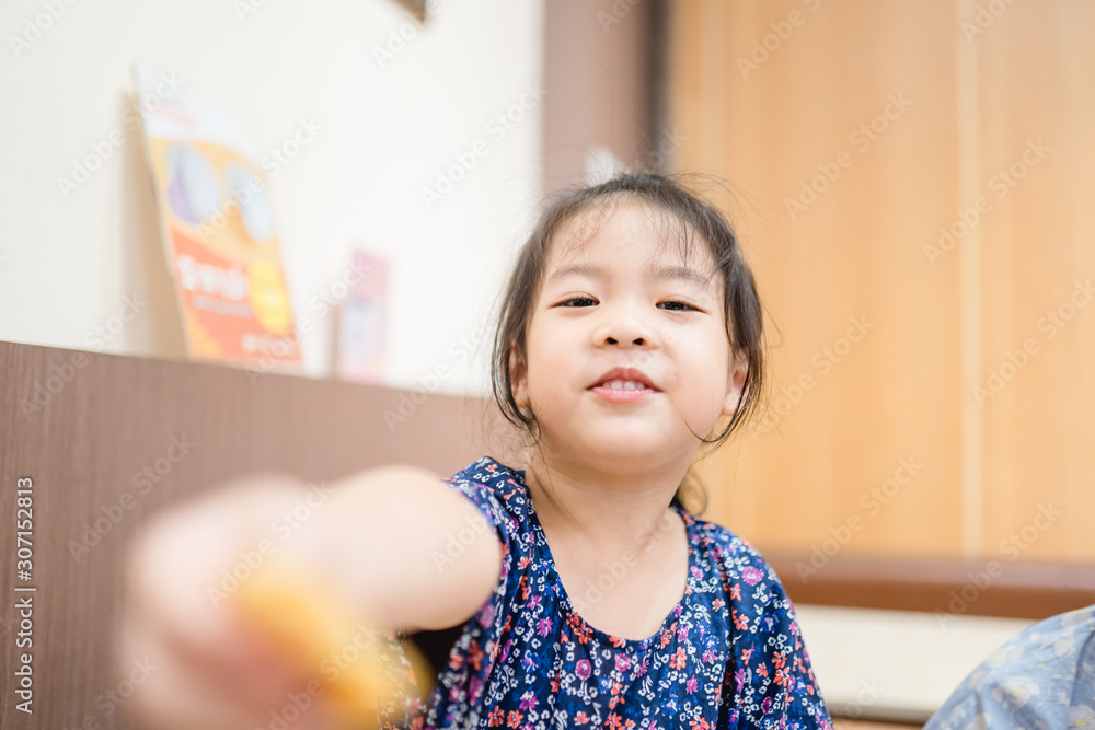 Wall mural Little asian child girl enjoy eating a crispy deep fried pork wonton in chinese restaurant with her hands.Happy time in lunch with asian food everyday.Delicious face and and enjoy eat concept.