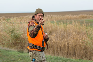 Hunting period, autumn season open. A hunter with a gun in his hands in hunting clothes in the autumn forest in search of a trophy. A man stands with weapons and hunting dogs tracking down the game.