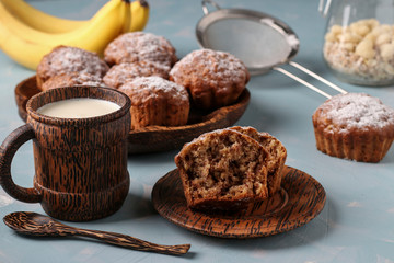 Banana muffins with oatmeal flakes sprinkled with icing sugar on a coconut plate and cup of milk, horizontal orientation