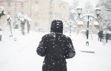 Man in black jacket walking in the street in cold snowy winter day - Powered by Adobe