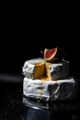 Close-up halfs of figs and cheese with honey on the black background