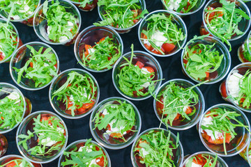 Mini appetizer salad in a glass of tomatoes with mozzarella, arugula and pesto. Italian traditional food for guests and participants at the event. Catering and guest services.