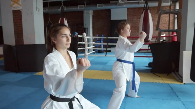 Medium shot of two young barefoot female karatekas practicing different punches in indoor gym