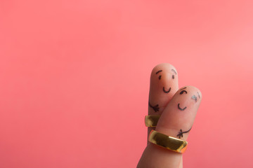 Painted happy fingers smiling in love against pink background with copy space for ad text. Marriage wedding rings