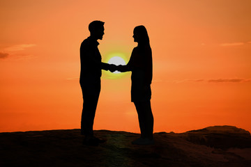 Silhouette of man and woman holding hands together at big sunset and romantic background