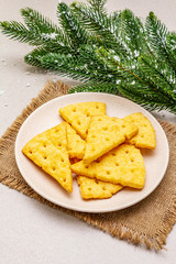 Festive cheese crackers, New Year snack concept. Cookies, fir tree branch, artificial snow, sackcloth napkin. Stone concrete background