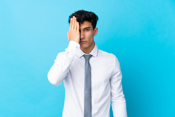 Young Argentinian businessman over isolated blue background covering a eye by hand