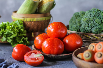 Photo of fresh tomatoes in a bowl on dark background around vegetables, carrot, salt, black pepper, corn, broccoli. Slice tomatoes. Harvesting tomatoes. Drops of water vegetables. Wooden table. Image