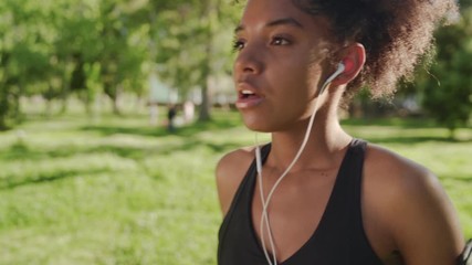 An african american young fitness woman taking breathe and inserts earphones in her ears before running in the park