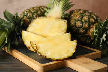Cutting board with pineapples on wooden background, close up