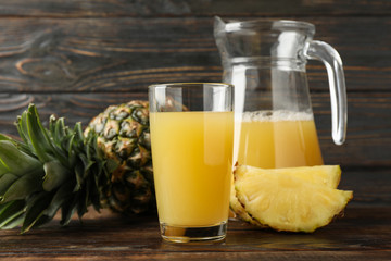 Pineapple, glass jug and glass with juice on wooden background, space for text